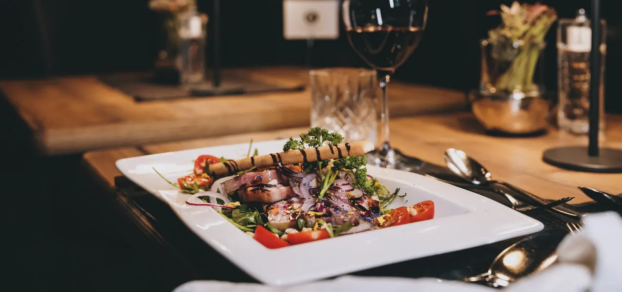 Ein Teller mit gegrilltem Fleisch, Gemüse und Salat, dazu ein Glas Rotwein.