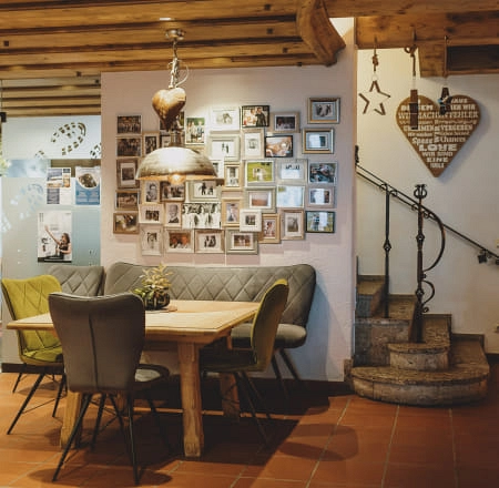 Gemütlicher Essbereich mit Holztisch, grünen und grauen Stühlen sowie einer Bilderwand