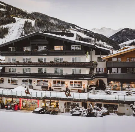 Exterior view of a hotel in the mountains, surrounded by snow and peaks.