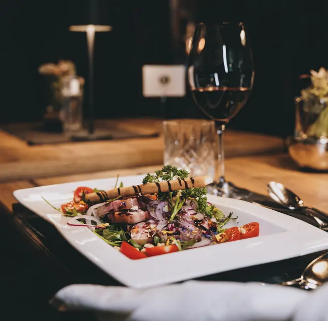 A plate with grilled meat, vegetables, and a glass of red wine.