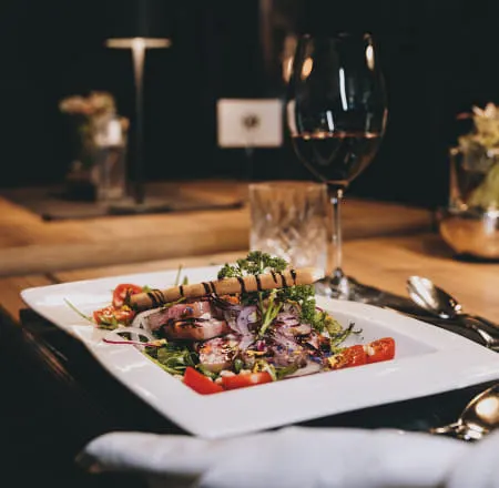 Gourmet dish on a plate with salad and wine in the background