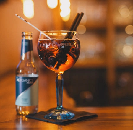 Cocktail in Glas mit Bombay Sapphire Logo und Flasche daneben