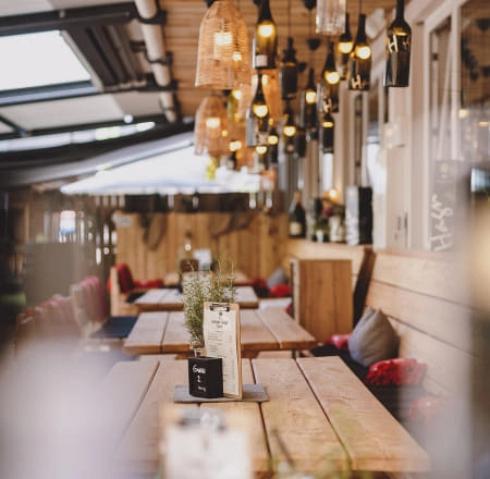 Gemütliche Lounge mit Holztischen und hängenden Lampen, Pflanzen und Menüs.