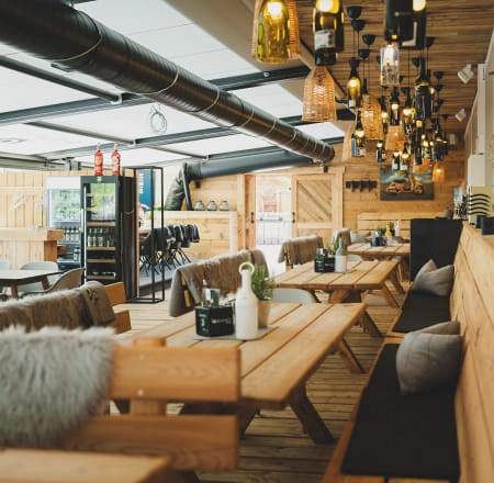Innenansicht eines Restaurants mit Holztischen und hängenden Lampen