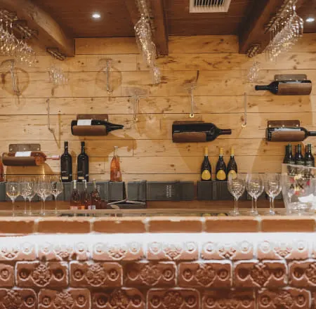 Weinbar mit Holzregalen und Weingläsern, hinter dem Tresen hängen Flaschen.