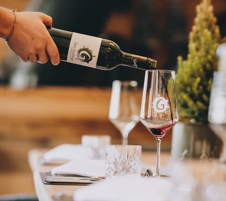 Weinflasche wird in Gläser mit G-Logo gegossen, gedeckte Tafel im Restaurant.