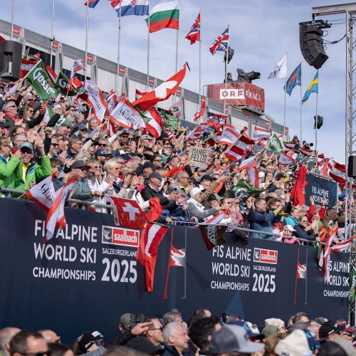Crowd celebrating at the Audi FIS Ski World Cup Final 2024 with flags and banners.