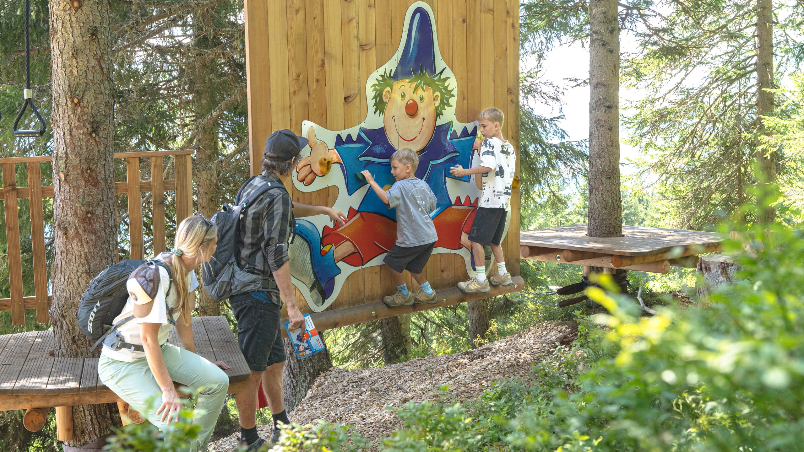 Children and adults explore the Montelinos Erlebnisweg with a character figure.
