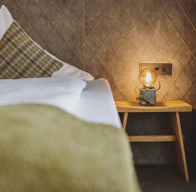 Detailansicht eines Bettes mit Kissen und Lampe auf einem kleinen Tisch