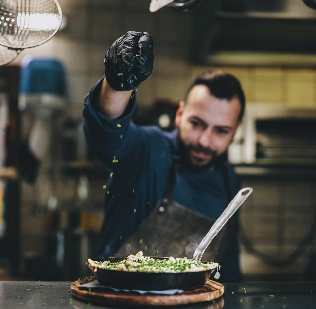 Chef seasoning a dish in a restaurant kitchen