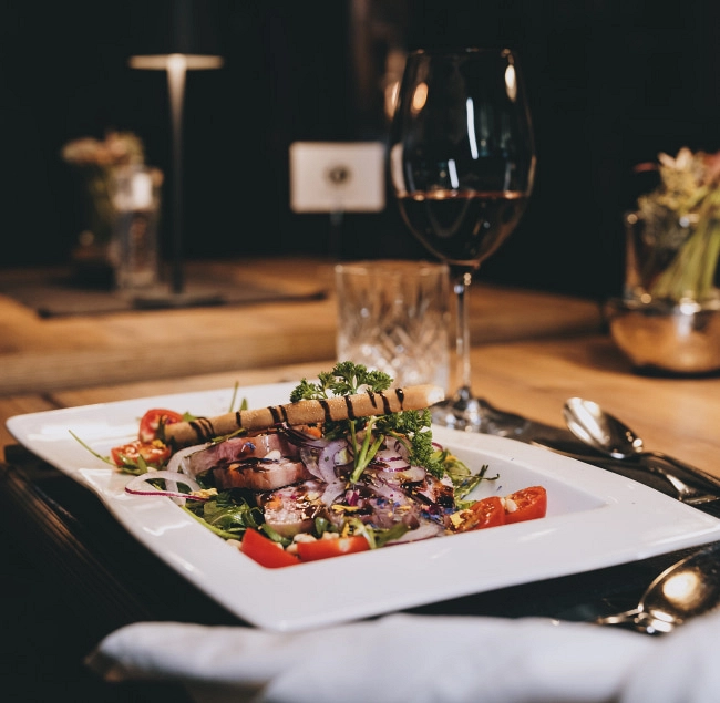 Gourmetplatte mit Fleisch, Salat und Gemüse, Weinglas im Hintergrund