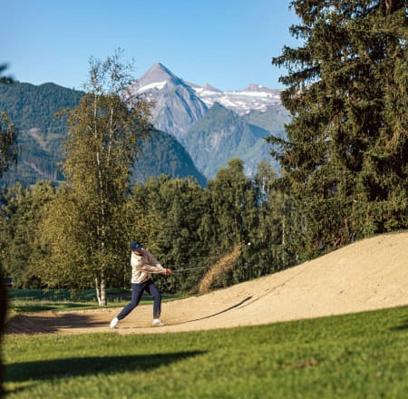 Golfer schlägt einen Ball aus einem Bunker mit Bergen im Hintergrund