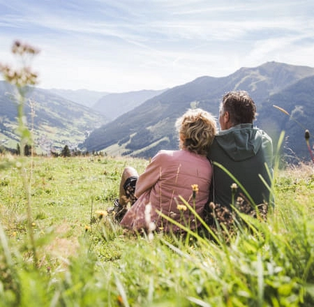 Paar sitzt auf einer Wiese und schaut auf die Berge in Saalbach Hinterglemm