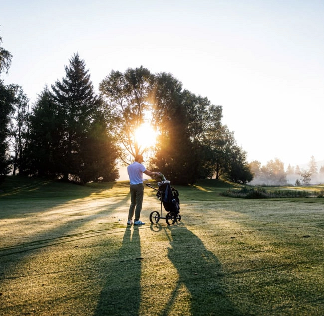 Mann mit Golftrolley beim Golfen in Zell am See, Sonnenaufgang im Hintergrund