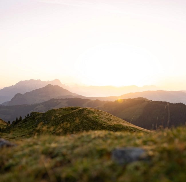Landschaft mit sanften Hügeln und Bergen im Hintergrund bei Sonnenuntergang