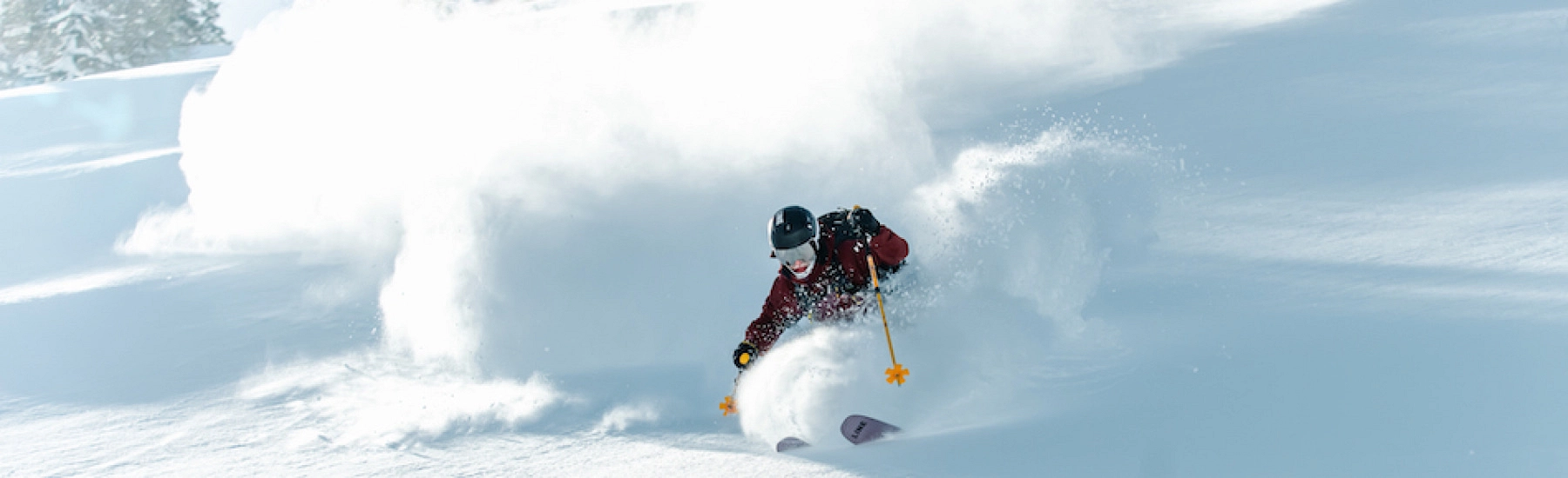 Skifahrer fährt durch tiefen Schnee mit Sprühnebel.