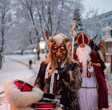 Person mit Maske und Trommel, Schnee, festliche Atmosphäre.
