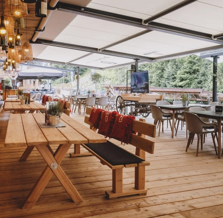 Gemütliche Terrasse mit Holztischen und modernen Stühlen, begrüntem Hintergrund.