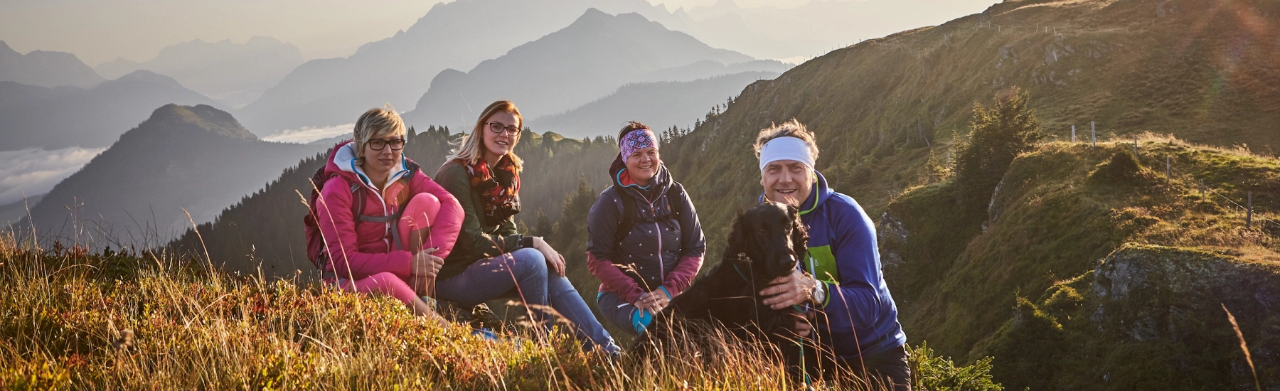 Gruppe von Wanderern, die auf Gras mit Bergen im Hintergrund sitzen