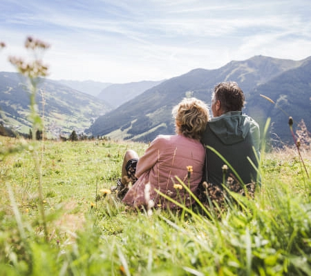 Paar sitzt auf einer Wiese und blickt auf die Berge in Saalbach-Hinterglemm