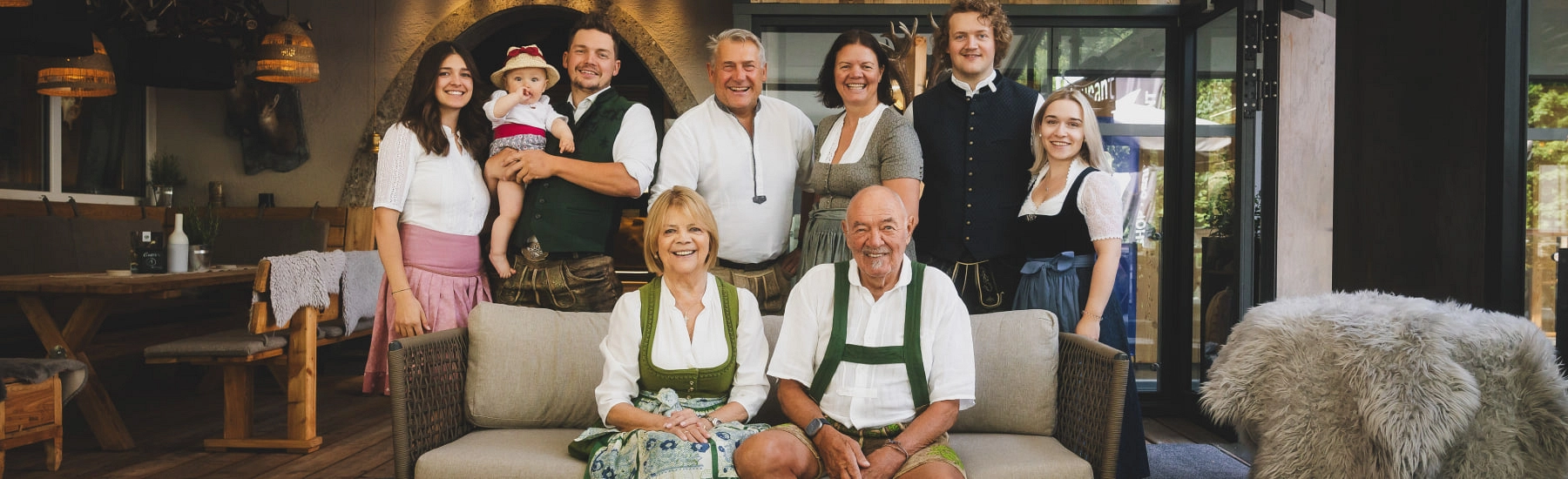 Familie posiert im Wohnzimmer, traditionelle Trachten und Baby auf dem Arm.