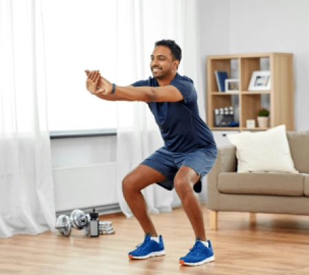 Mann macht Hocke in einem hellen Raum mit Hanteln im Hintergrund