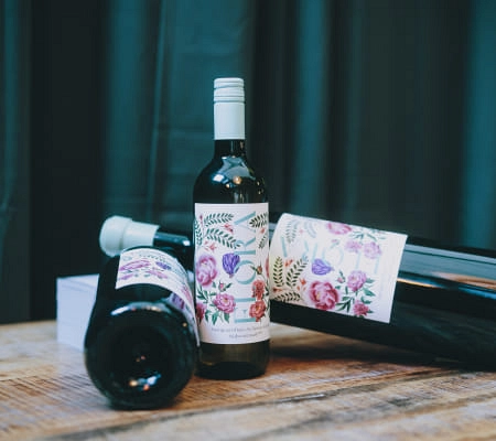 Drei Weinfalschen mit floralen Etiketten auf einem Holztisch.