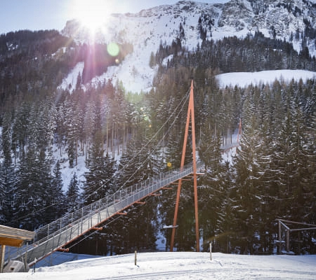 Hängebrücke im Schnee mit Bergen im Hintergrund