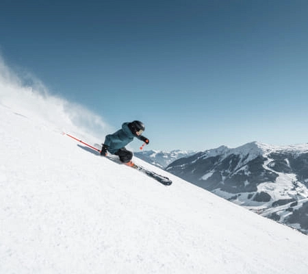 Skifahrer fährt die Piste in Saalbach-Hinterglemm, mit Bergen im Hintergrund.