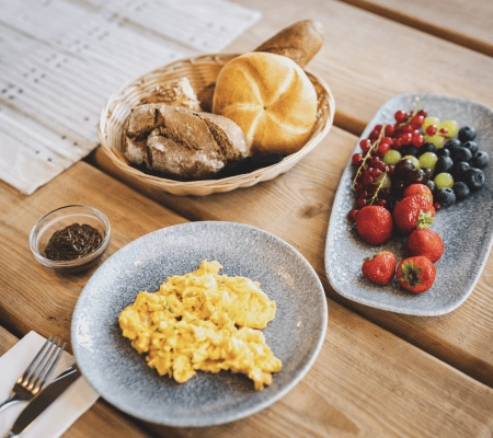 Frühstückstisch mit Rührei, Brot, Früchten und einer kleinen Schale Marmelade
