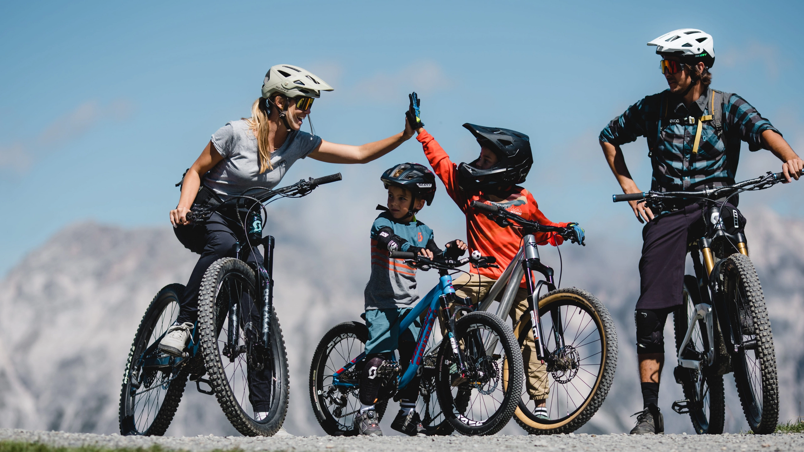 Family biking in the mountains, kids high-fiving.